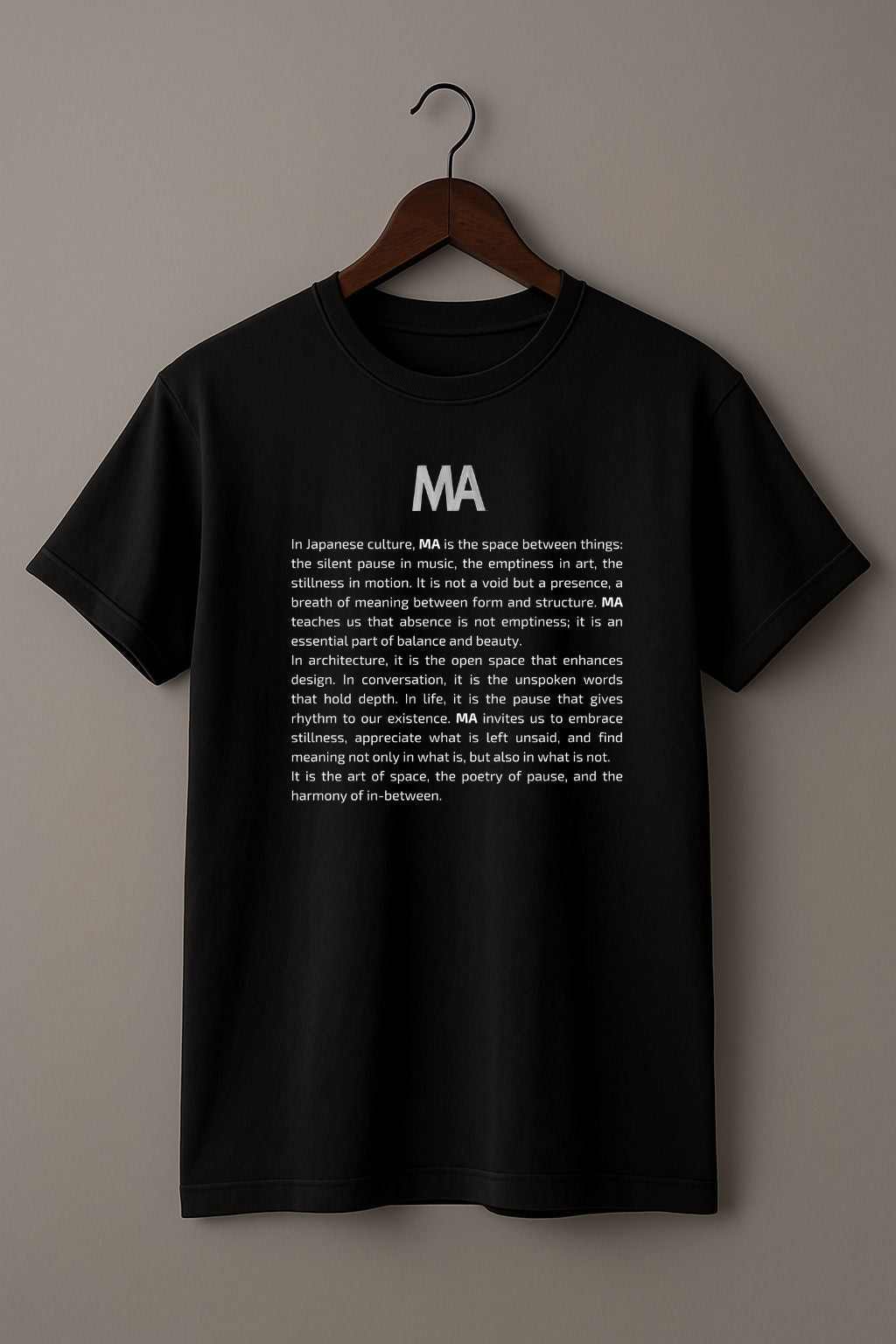 Black t-shirt with white text Ma and its concept on a hanger against a beige background