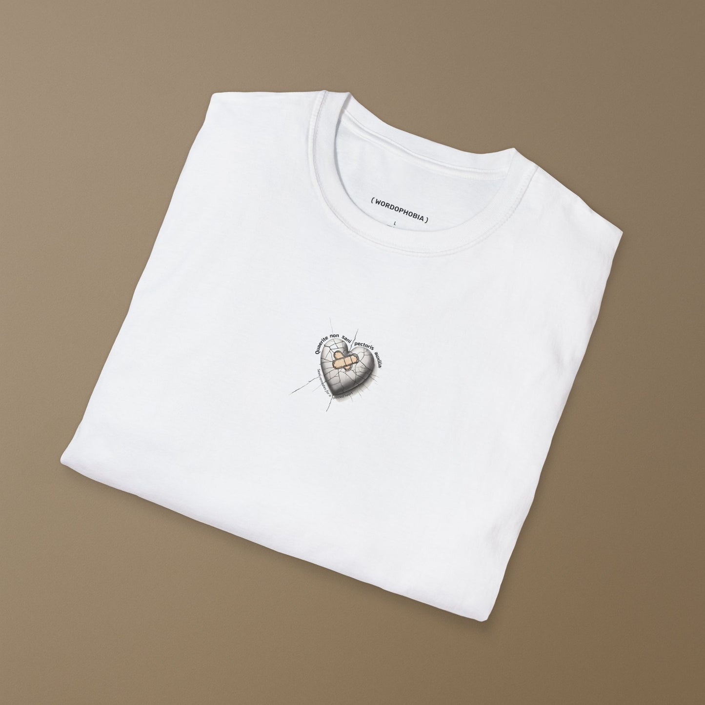 Folded white T-shirt with a small white patch featuring a design of heart with a bandage and cracked surface, featuring the Latin phrase “Quaerite non sani pectoris auxilia,” meaning “Seek remedies for a sick heart,” on a brown background