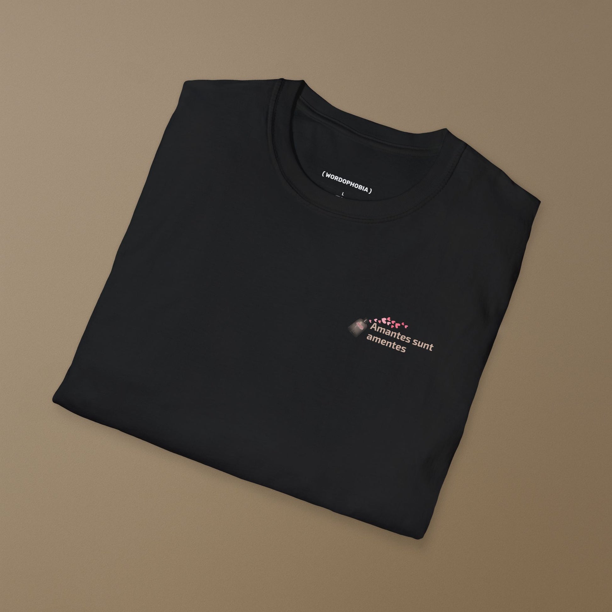 Folded black t-shirt with a with a small design of a Latin phrase "Amantes sunt amentes"  and small graphic of hearts  on a brown background 
