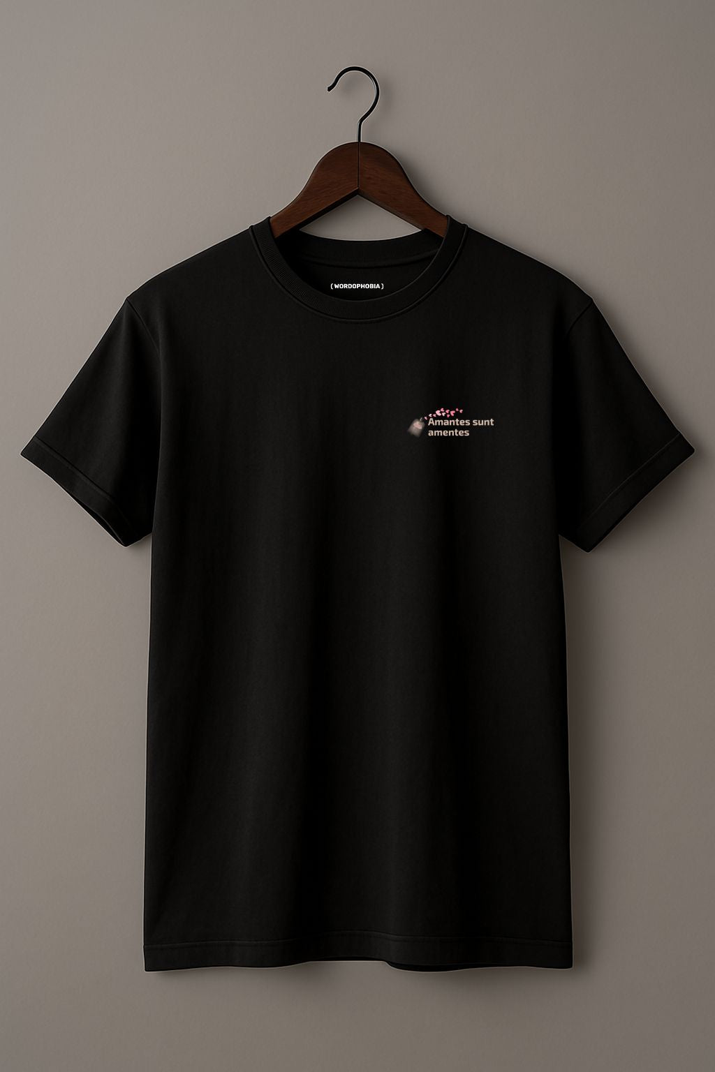 Black t-shirt with a small design of a Latin phrase "Amantes sunt amentes"  and small graphic of hearts on a wooden hanger against a plain background