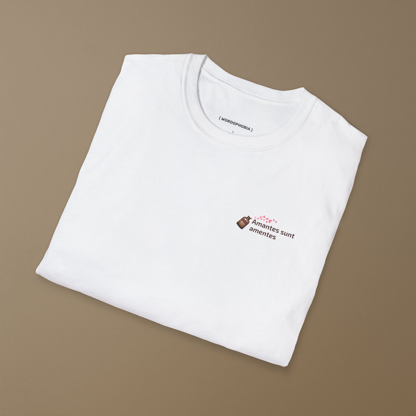 Folded white t-shirt with a with a small design of a Latin phrase "Amantes sunt amentes"  and small graphic of hearts  on a brown background 