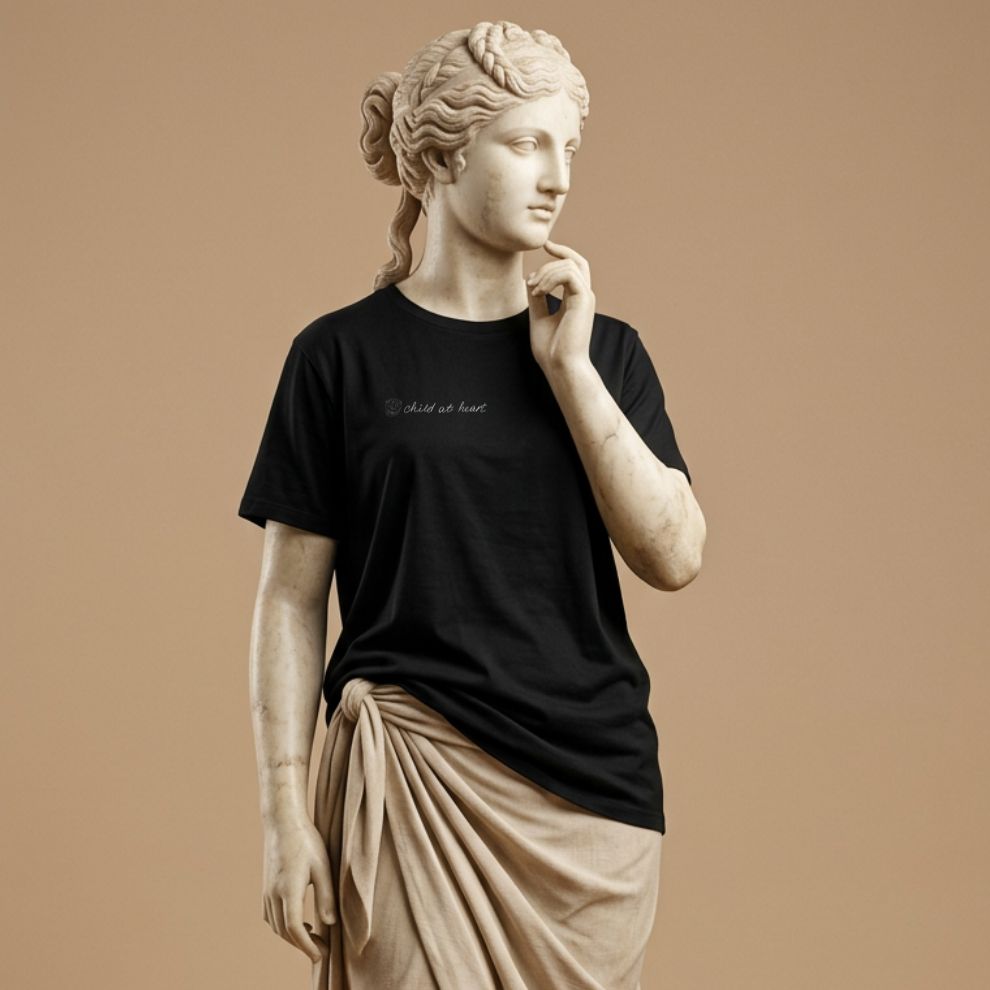 Statue wearing a black t-shirt with graphic design of hand drawn kids picture of the funny face and the hand written text "child at heart" on a beige background