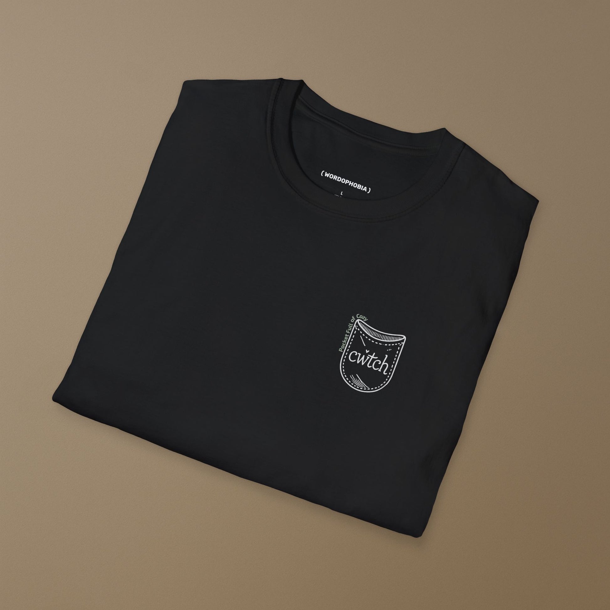 Folded black t-shirt with a small graphic design of a tiny pocket with 'cwtch' word and text "Pocket Full of Cozy" on a beige background