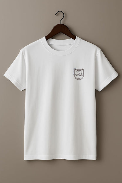 White t-shirt with a small graphic design of a tiny pocket with 'cwtch' word and text "Pocket Full of Cozy" on a wooden hanger against a plain background