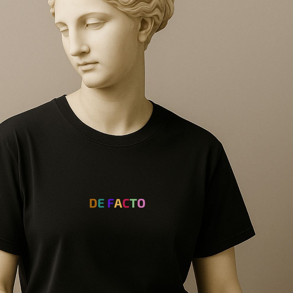 Black t-shirt with 'DE FACTO' in colorful letters worn by a statue.
