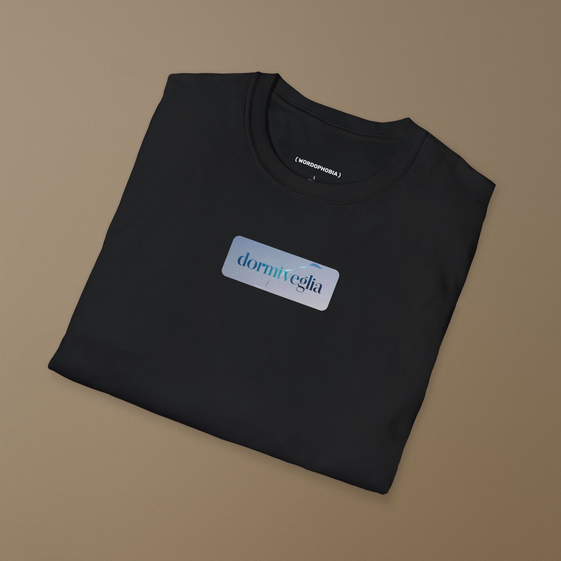 Folded black T-shirt with the word dormiveglia, symbolizing the state between sleep and wakefulness with a calm design on a plain beige background