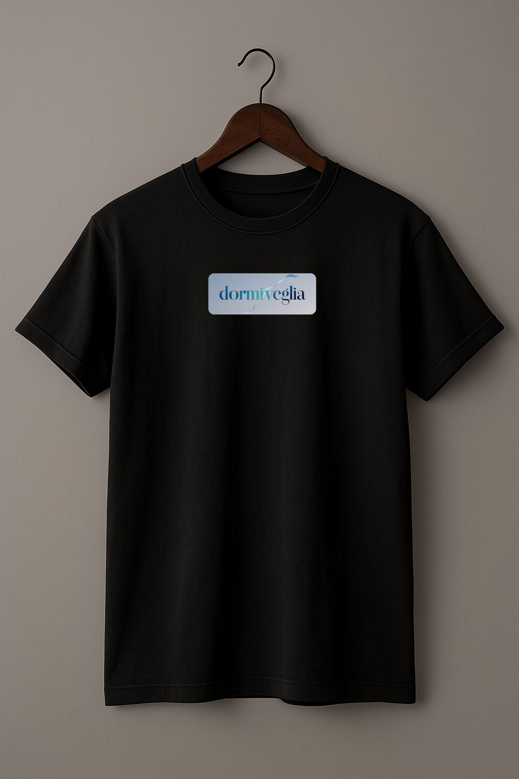 Black T-shirt with the word dormiveglia, symbolizing the state between sleep and wakefulness with a calm design on a wooden hanger against a plain beige background