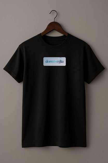 Black T-shirt with the word dormiveglia, symbolizing the state between sleep and wakefulness with a calm design on a wooden hanger against a plain beige background