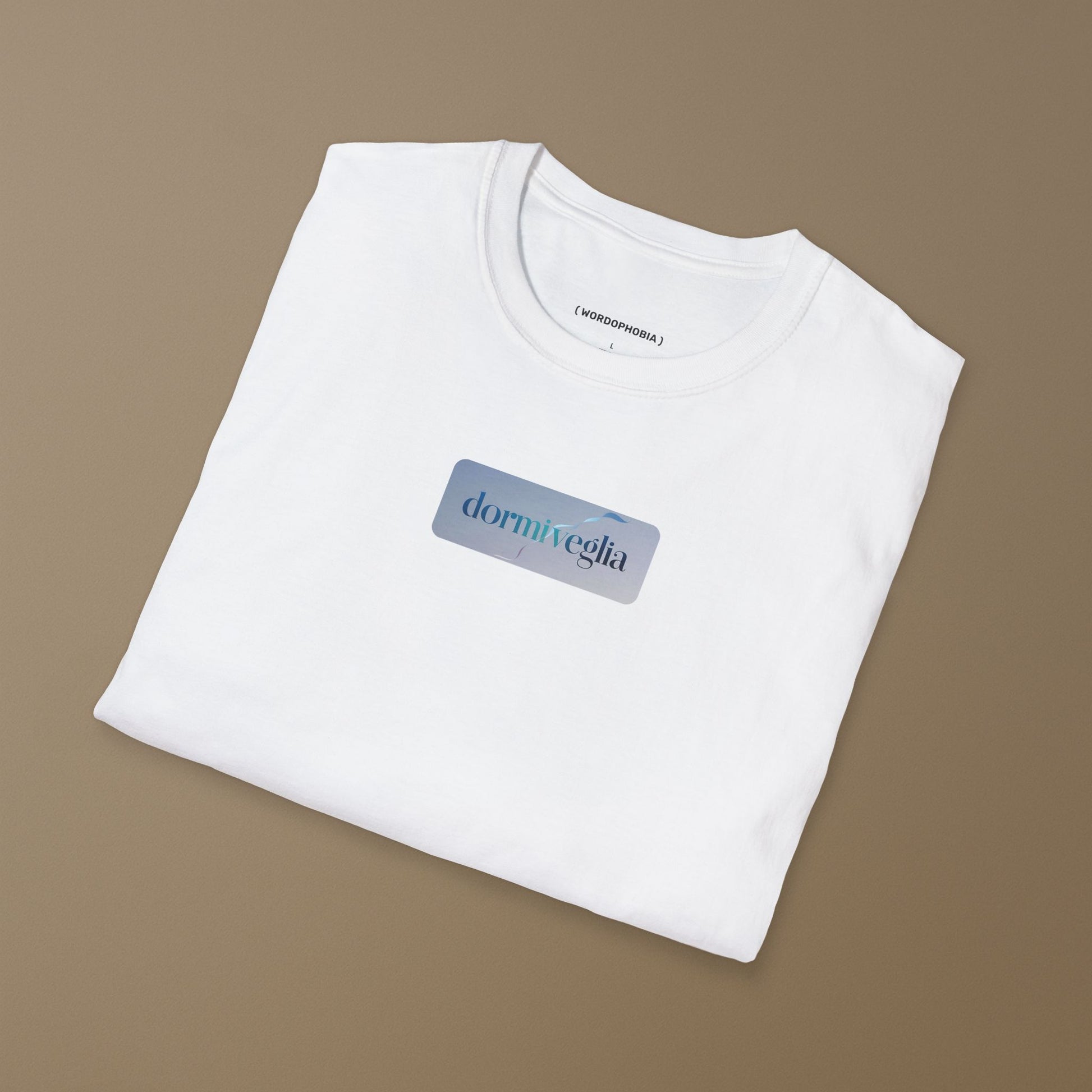 Folded white T-shirt with the word dormiveglia, symbolizing the state between sleep and wakefulness with a calm design on a plain beige background
