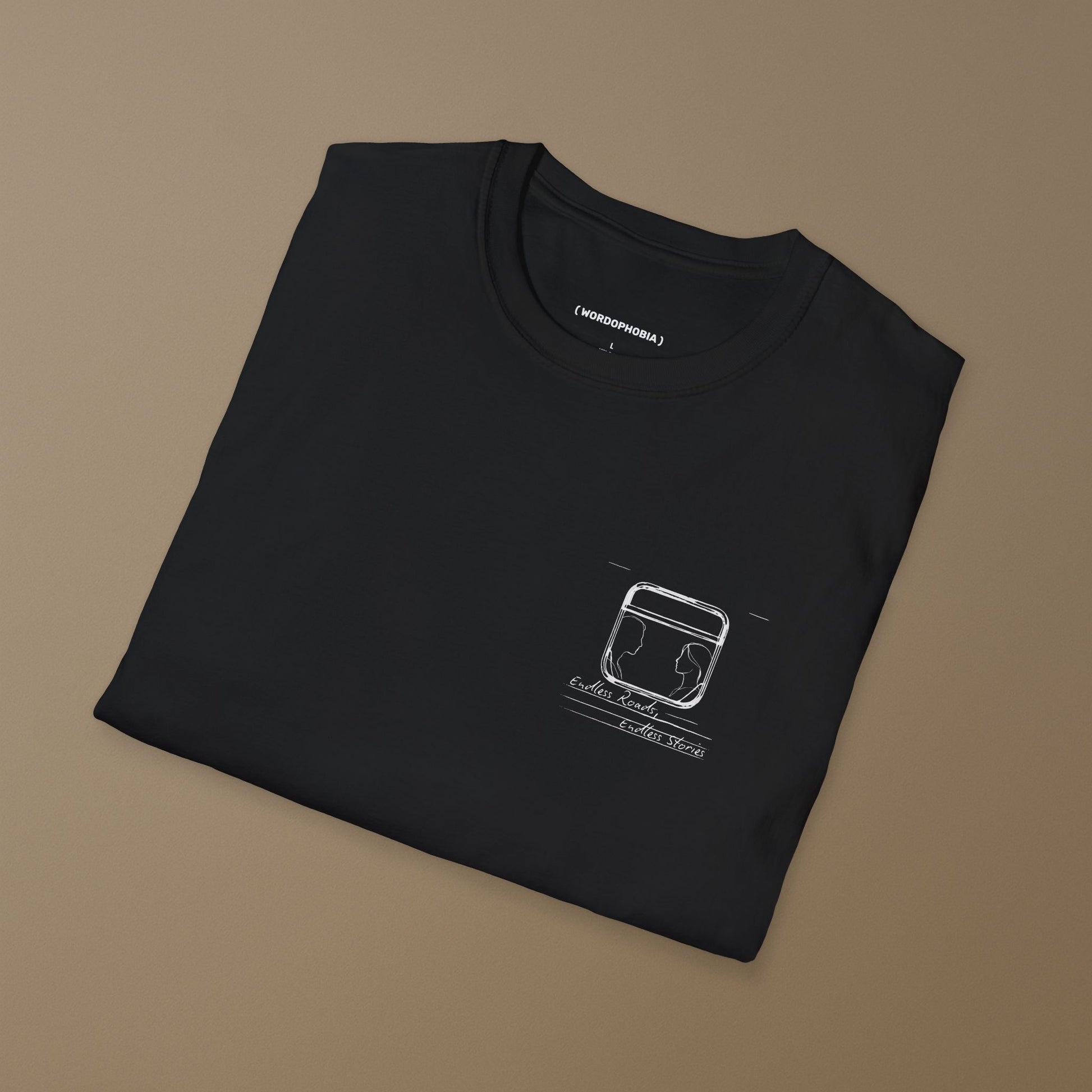 Folded black t-shirt with a graphic minimalist design of a train window with 2 silhouettes and handwritten text "Endless Roads, Endless Stories" on a beige background