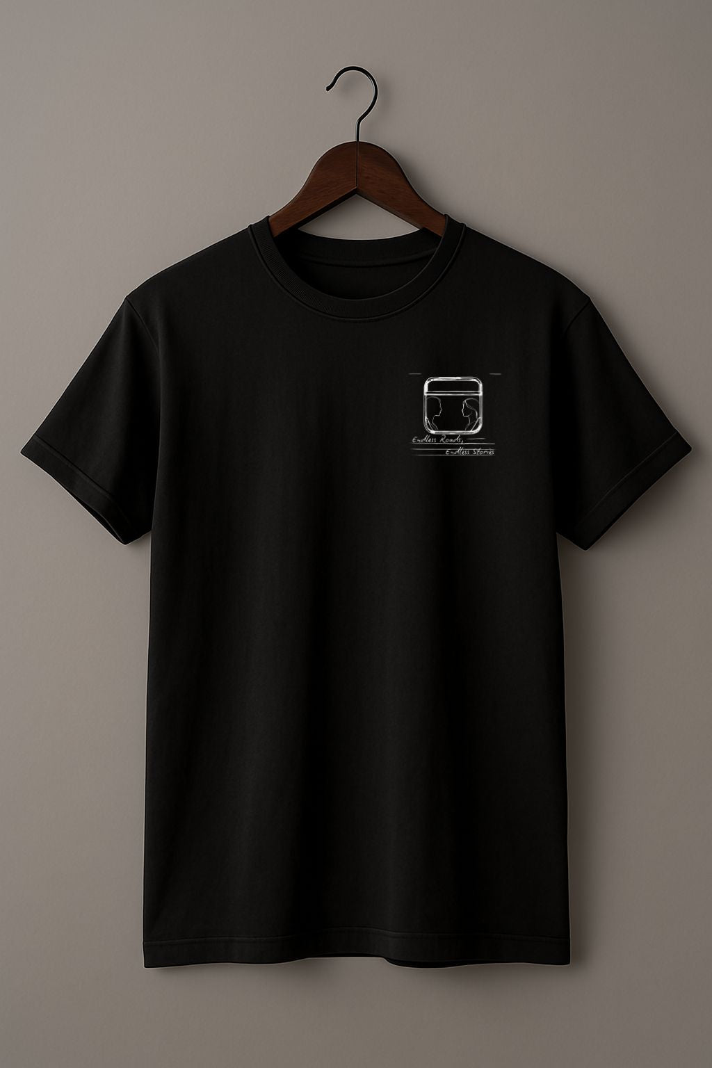 Black t-shirt with a graphic minimalist design of a train window with 2 silhouettes and handwritten text "Endless Roads, Endless Stories" on a hanger against a beige background