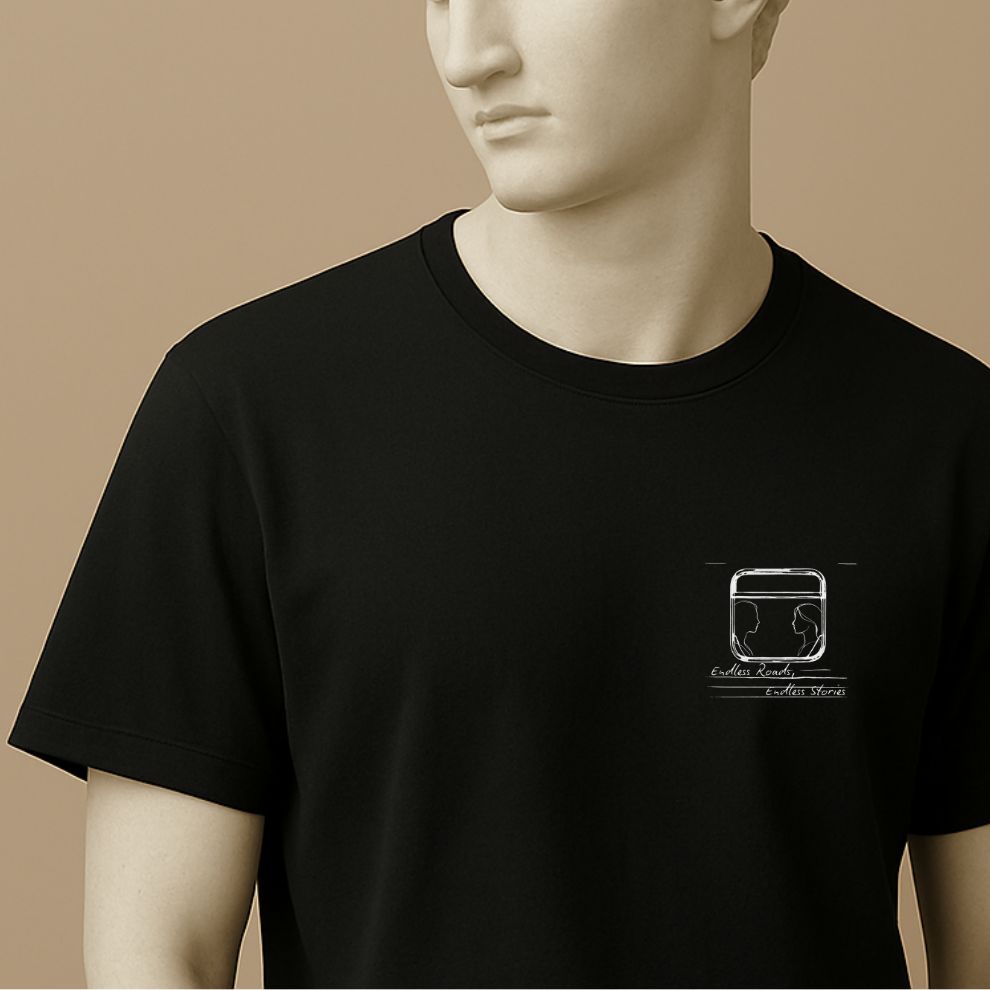 Statue wearing a black t-shirt with a graphic minimalist design of a train window with 2 silhouettes and handwritten text "Endless Roads, Endless Stories" 