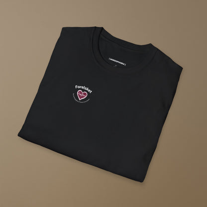 Folded black T-shirt with a design of a heart with a beat and texts  "Forelsket" and "The thrilling glow of love's first bloom" on a brown background