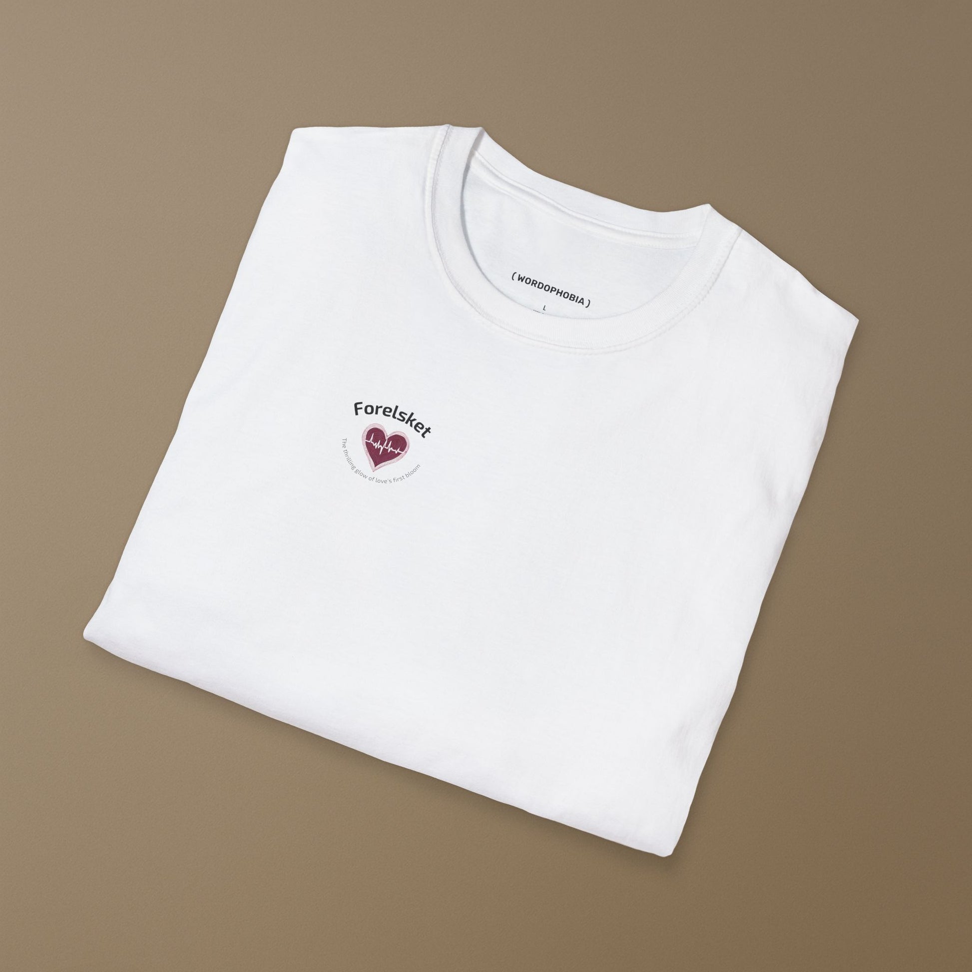 White t-shirt with a small design of a heart with a beat and texts  "Forelsket" and "The thrilling glow of love's first bloom" on a brown background