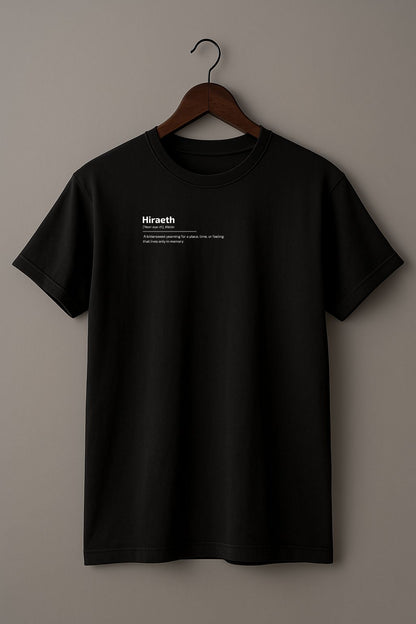 Black t-shirt with graphic design of the word HIRAETH ([ˈHeer-eye-th], Welsh) and its definition "A bittersweet yearning for a place, time, or feeling that lives only in memory" on a wooden hanger against a plain background