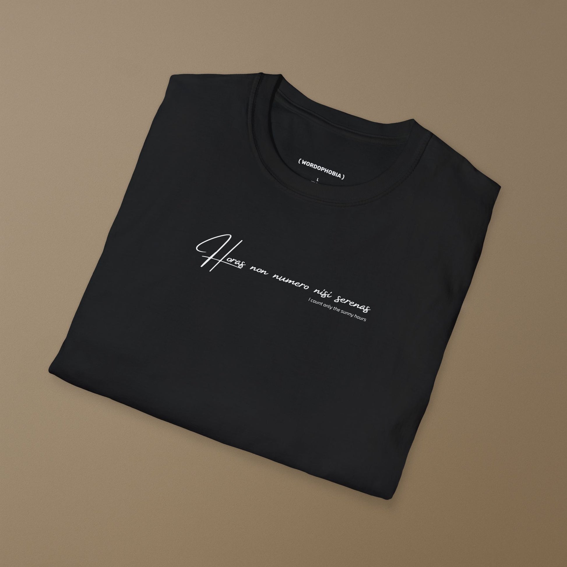 Folded black t-shirt with white Latin phrase "Horas non numero nisi serenas" on a brown background