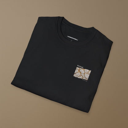 Folded black t-shirt with a small graphic of Kintsugi art with gold repair on a cracked white surface, text 'Kintsugi The art of healing' above on a brown background