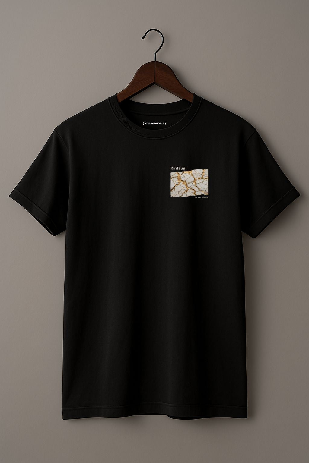 Black  t-shirt with a small graphic of Kintsugi art with gold repair on a cracked white surface, text 'Kintsugi The art of healing' above on a hanger against a beige background