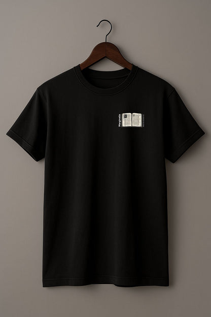 Black t-shirt with a small graphic of Enlarged design of open old book with text "Marginalia" and "Where the real ideas live" on a hanger against a beige background