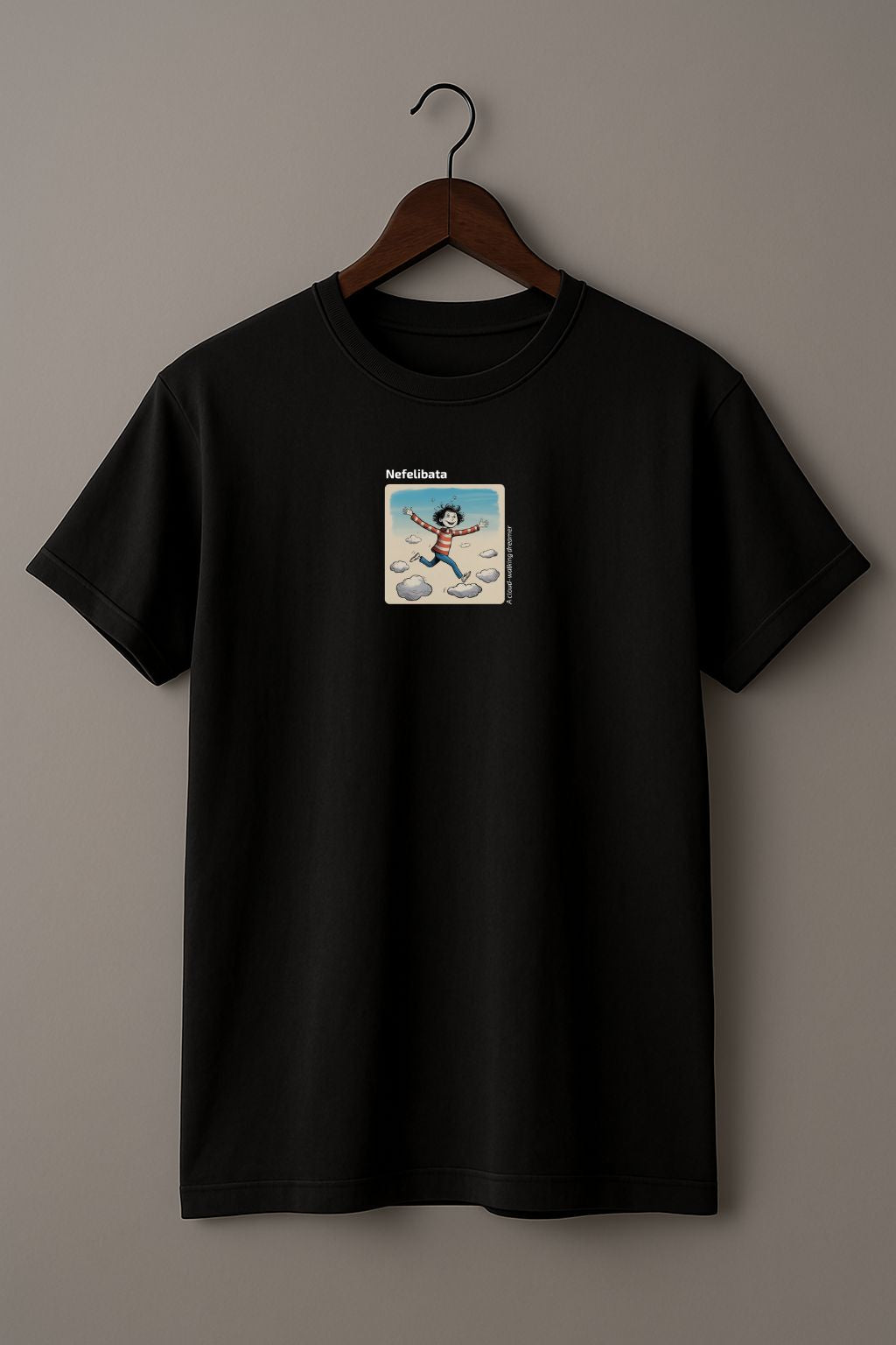 Black t-shirt with a graphic design of a  funny child running on clouds with 'Nefelibata' text and phrase "A cloud-walking dreamer" on a hanger against a beige background