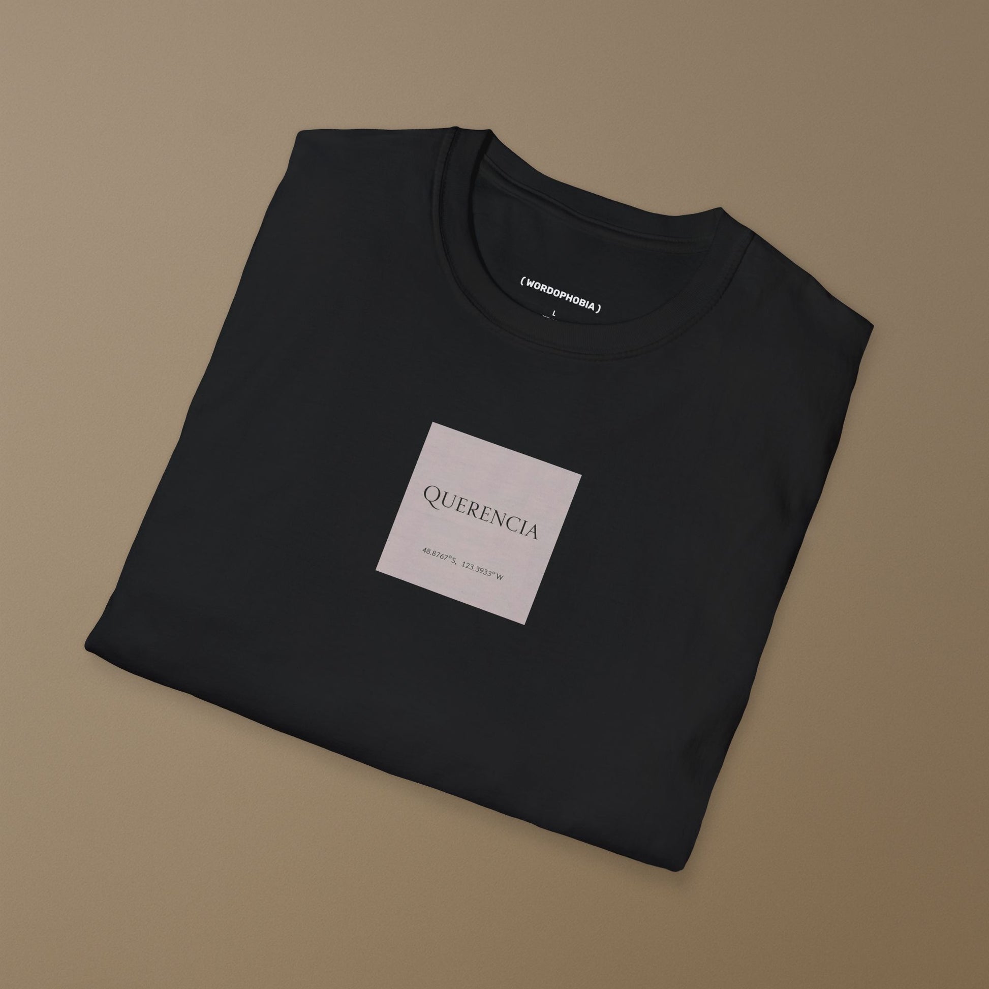 Black folded t-shirt with a pink label of the name 'Querencia' and geographical coordinates  on a plain background
