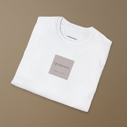 White folded t-shirt with a pink label of the name 'Querencia' and geographical coordinates  on a plain background