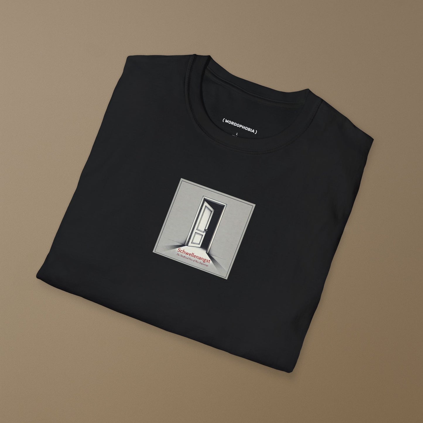 Folded black t-shirt with the German word “Schwellenangst,” meaning fear before a new beginning on a beige background