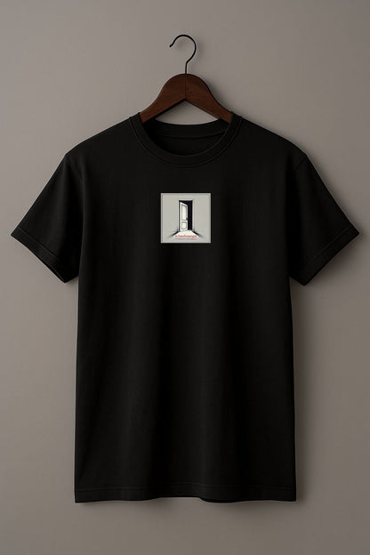 Minimalist black t-shirt with the German word “Schwellenangst,” meaning fear before a new beginning on a wood hanger against a beige background