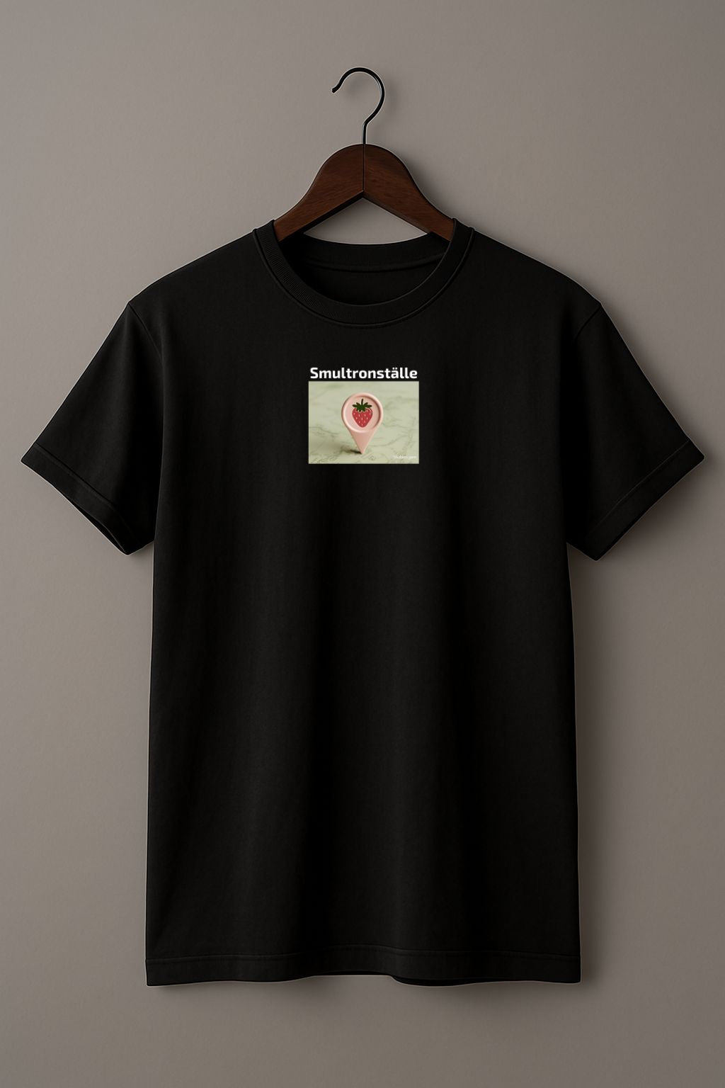 Black t-shirt with a graphic design of a map marker with strawberry design and text 'Smultronställe' on a light background on a hanger against a plain background