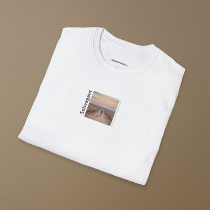 Folded white t-shirt with the word “Solivagant,” text “Drifting alone, finding the world,” and watercolor art of a lone traveler walking between hills on a beige background
