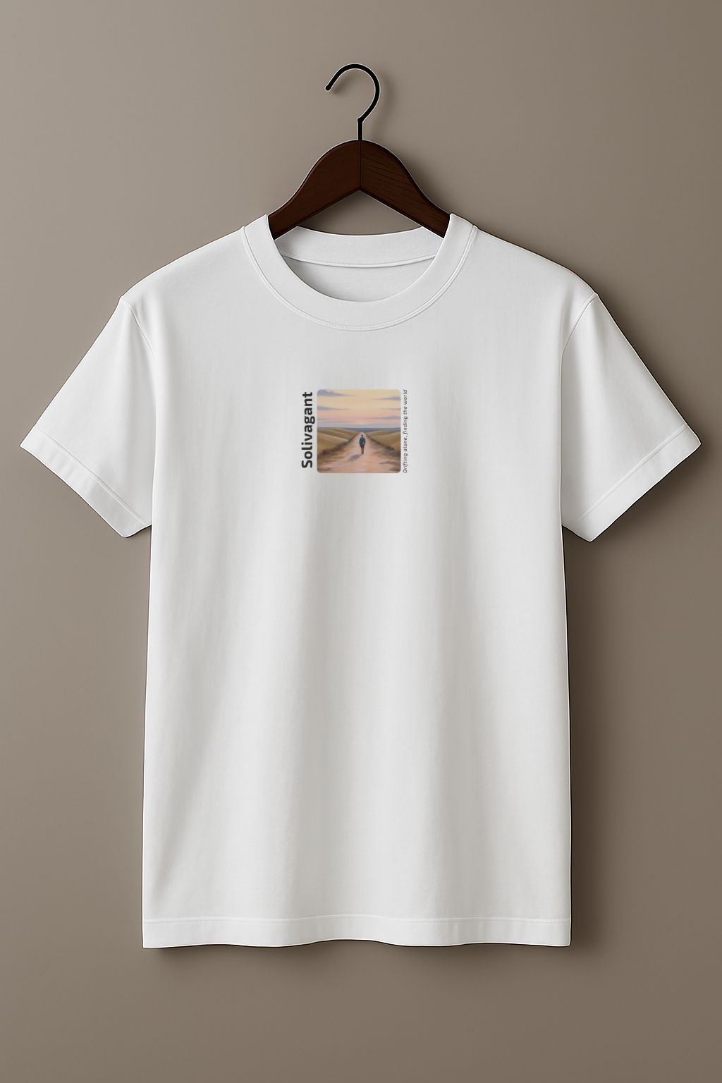 White T-shirt with the word “Solivagant,” text “Drifting alone, finding the world,” and watercolor art of a lone traveler walking between hills on a wood hanger on a beige background